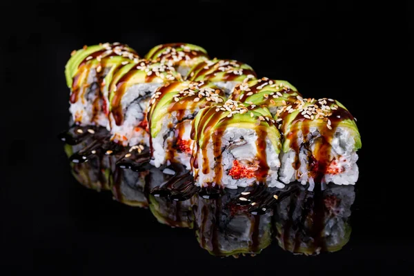 Roll with eel, rice, avocado, sesame seeds, sauce and Philadelphia cheese on a black mirror background