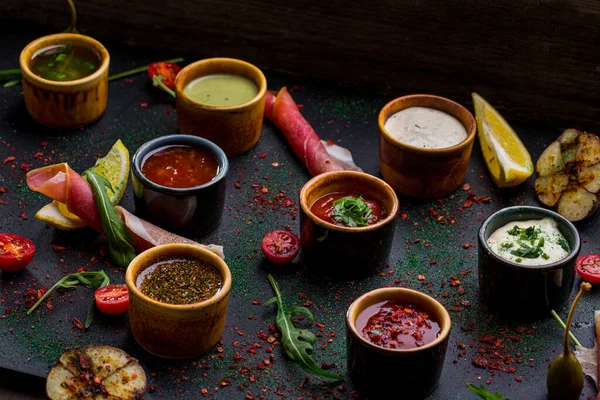 Doğu ve Kafkas mutfağı için sekiz farklı sos çeşitlendirdim. Soslar seramik sosların içinde. Uçan daireler siyah tahtada. Yanında prosciutto, vişneli domates, ızgara sarımsak, kapari, roka yaprağı, bir dilim limon ve baharat var.