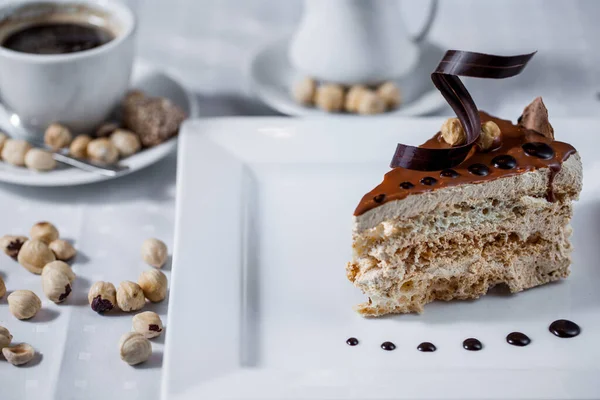Waffle tabaklı bir dilim pasta çikolata jölesi, fındık, beyaz tabakta çikolata parçacıkları ve bir kupa kahve ve krema. Yatay yönelim