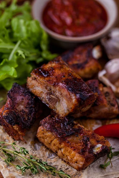 Grilled pork ribs marinated with cherry sauce, lay on pita bread with thyme and chili. Lettuce is next to it. Beige saucer with adjika stands behind.