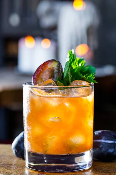 Erikli, naneli ve buzlu bir kokteyl, yanan mumların arka planında, ahşap bir masanın üzerinde duruyor.