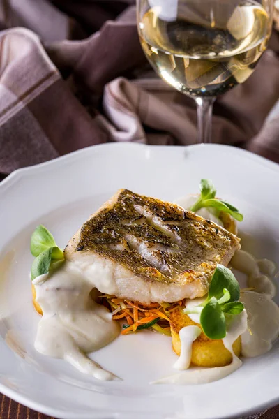 Grilled sea bass steak with white sauce, Korean carrots, mung bean salad, on a white plate with a glass of wine. Vertical orientation 