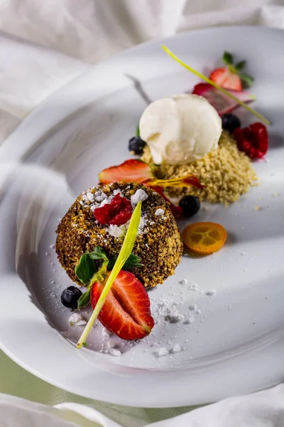 Dessert fudge with strawberries, raspberries, blueberries, kumquat, mint flower petals and powdered sugar on a white plate and light background. Vertical orientation