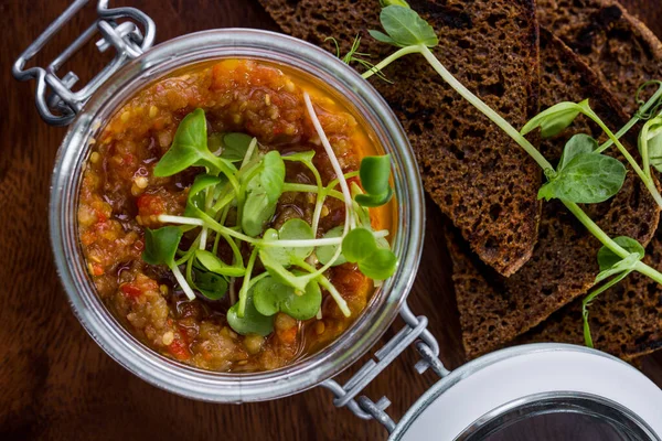 Eggplant caviar with pea sprouts in a jar and fried bread on a wooden table