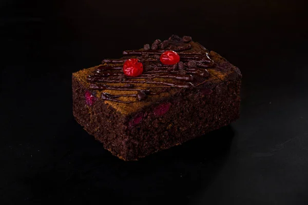 Chocolate brownie with cranberries and chocolate drops on a black background. Horizontal orientation