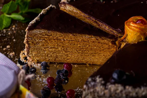 A piece of honey cake in chocolate glaze with currants, mint and cranberries on a wooden table. Vertical orientation