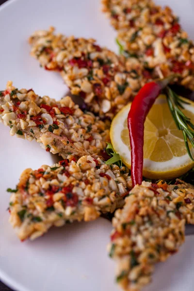 Fıstıkta pişirilmiş mürekkep balığı, yeşillik ve kırmızı biber ekmeği. Beyaz, derin bir tabakta, roka ve marul salatası karışımı bir tabağın üzerinde bir dilim limon ve kırmızı biber var..