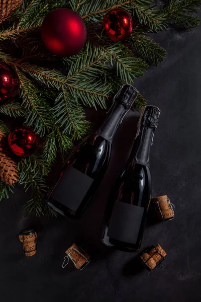Köknar dalları ve Noel süslemeleri ile siyah bir masanın üzerinde duran mantarlı şampanya şişeleri.