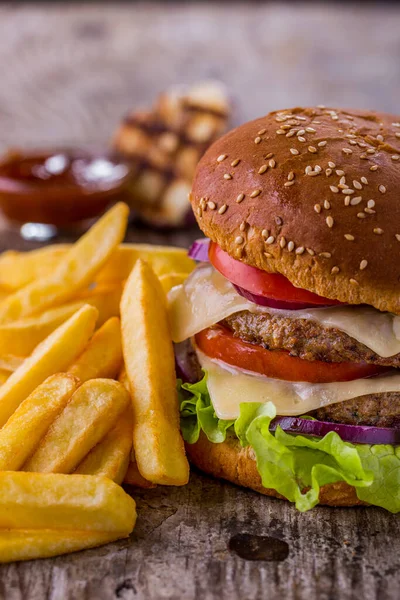Burger with sesame bun, double cutlet, tomatoes, onions, lettuce, double cheese and mayonnaise with fries, garlic and sauce on a wooden table. Vertical orientation