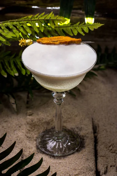 Cocktail with dried fruit on a stick and froth in a glass standing on bricks