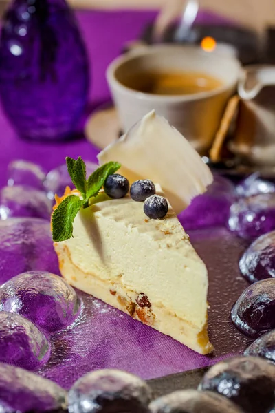 Cheese casserole with raisins, blueberries and mint on a purple table and a cup of tea. Vertical orientation