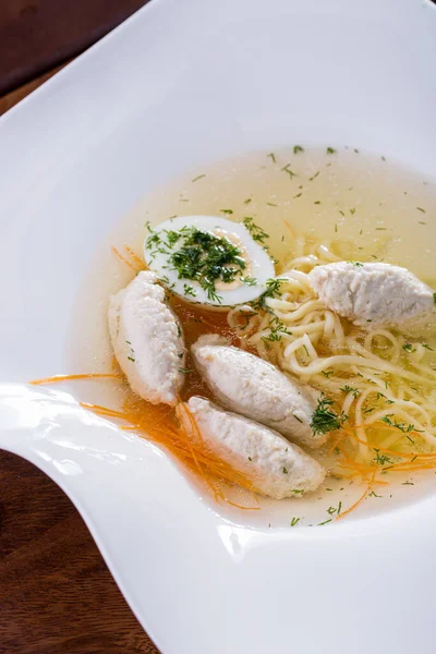 Soup with boiled egg, meat balls, noodles in a plate on a wooden background