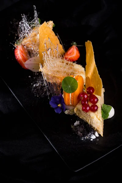 Makarna, çiçek yaprakları, cips, çilek, şeker iplikleri, kırmızı frenk üzümü ve siyah bir tabakta naneli şeker parçaları. Dikey yönelim