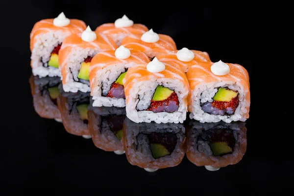 Roll with salmon, scallops, cucumber, rice, nori, mayonnaise, avocado and tobiko caviar on a black mirror background