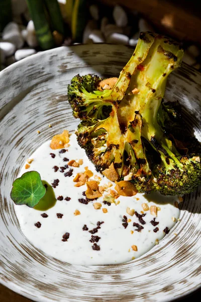Fried broccoli with sauce, chopped garlic peanuts and candied fruits in a plate against the background of a plant in a box