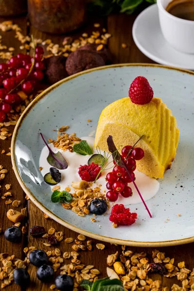 cottage cheese casserole with raspberries, red currants, blueberries, mint leaves and oatmeal flakes. Stands on a blue ceramic plate. The plate stands on a wooden table, strewn with cereals, nuts and berries. On the table is a can of sour cream and j