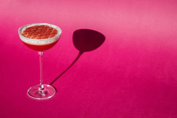 Buzlu, köpüklü ve pembe arka planda duran bardakta kırmızı serpiştirilmiş kokteyl.