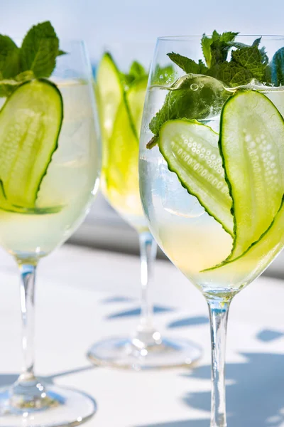 Three cocktails with ice, cucumbers and mint in glasses that are on the table against the background of blue sky and water