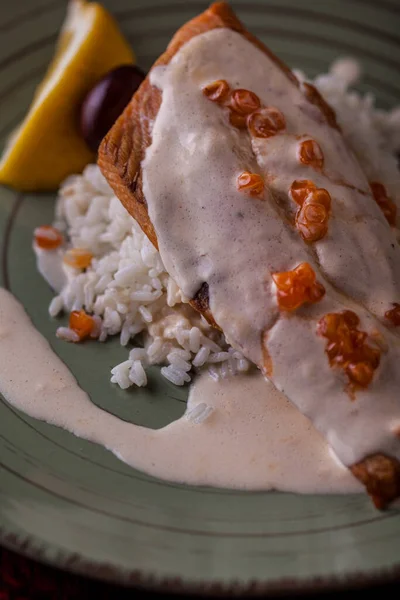 Pirinçli, zeytinli, limonlu ve havyarlı kızarmış somon dilimleri yuvarlak tabakta ve ahşap zemin üzerinde. Dikey yönelim