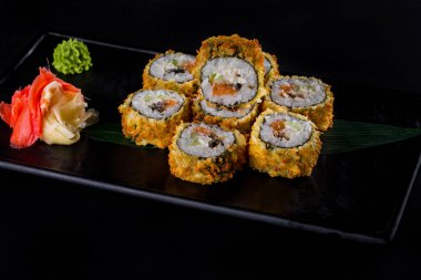 Warm rolls in batter with salmon, eel, avocado, nori and Philadelphia cheese in a plate with wasabi and pickled ginger on a black background