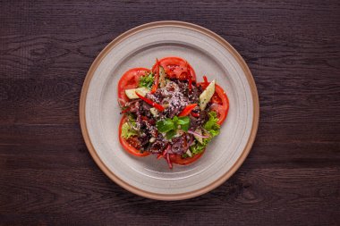 Salad with meat, lettuce, cucumbers, onions, sesame seeds, endive, mint, tomatoes and arugula in a plate on a wooden background