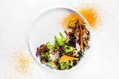 Salad with walnut pieces, dried apples, mushrooms, lettuce, green pea sprouts, flower petals and curry seasoning in a plate on a white background