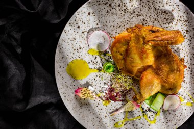 Baharatlı kızarmış tavuk ve ballı hardal sosu, lahanalar, turplar, salatalık ve çiçek yaprakları beyaz yuvarlak tabakta. Yatay yönelim