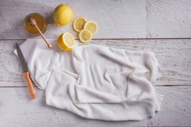 Sliced and whole lemons with honey in a bowl and a towel on a wooden table