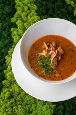 Zarzuela çorbası, bitki, susam tohumu, et ve karides ile yeşil arka planda bir tabakta
