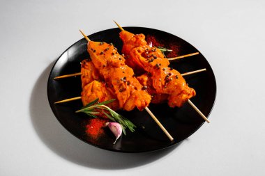 Fried chicken meat with sauce on skewers with peppercorns, paprika, salt, rosemary and garlic in a plate on a white background