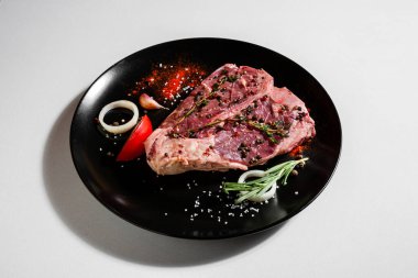 Raw pork meat on the bone with peas, tomatoes, onions, paprika, salt, rosemary, thyme and garlic in a plate on a white background