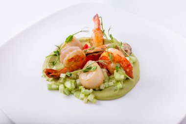 Salatalıklı bezelye ezmesi yastığında sarımsak ve zeytinyağında kızartılmış karides. Üstte mikroyeşil filizler var. Yemek beyaz, düz tabakta. Beyaz arkaplan.