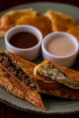 Soslu beyaz ve kırmızı soslu etli turta, yuvarlak tabakta samsa. Dikey yönelim 