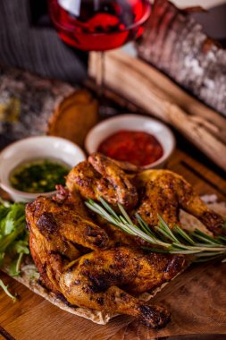 Sarımsak soslu ızgara tütün tavuğu. Yakınlarda bir çatal ve bir bıçak, sarımsak soslu ve satsibeli soslu bir sos kabı var. Tavuk bir tabak pide ekmeğinin üzerinde yatıyor. Lavaş ve çatal bıçak seti ahşap bir tahtanın üzerinde, yanında bir bardak r var.