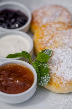 Beyaz tepside pudra şekerli krep kayısı reçeli, ekşi krema ve siyah frenk üzümü reçeli beyaz çay tabağı ve naneli. Tabak, demir ağacı çalılarının arasındaki ağaç kabuğunda duruyor..