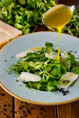 Salad with cheese, mung bean salad, flower sprouts in a plate on a wooden table with salad, a large piece of cheese and a spoonful of sauce