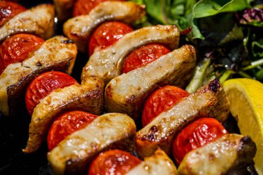 Kebab with slices of mackerel, cherry tomatoes, slice of lemon and basil on a black plate on the grass. Horizontal orientation 