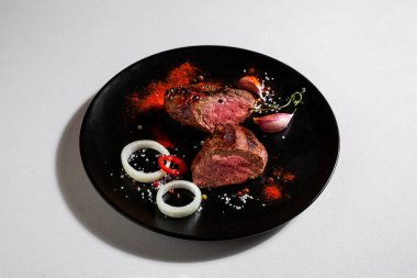 Pieces of fried pork steak with peppercorns, onions, paprika, salt, thyme and garlic in a plate on a white background