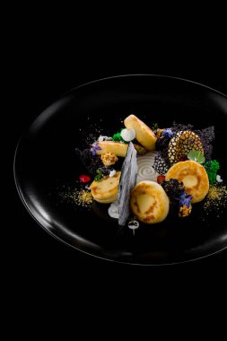 Ekşi kremalı, naneli, mikro yeşil, böğürtlenli, ahududulu ve yenilebilir yapraklı peynirli kekler. Siyah bir levhada yatıyorlar. Siyah bir arkaplanda.