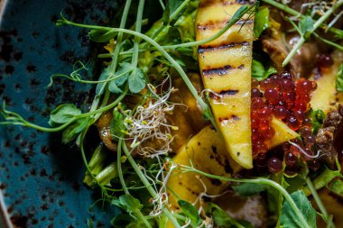 Salad with meat, fried mango, caviar, young shoots, pea sprouts, salad and mung bean salad in a plate on a wooden background with a glass of wine