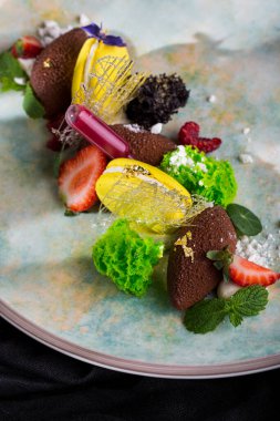 Macaroni with viper, mint, strawberries, powdered sugar, flower petals, sugar threads and gold leaf on a round plate. Vertical orientation