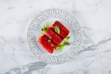 Philadelphia peyniri, kapari ve fesleğen yapraklı kırmızı biber turşusu. Aperatif yuvarlak, gümüş desenli beyaz bir tabakta. Tabak mermer bir yüzeye yerleştirilmiş..