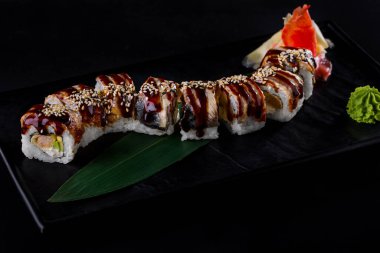 Rolls with shrimp, eel, sesame seeds, nori, avocado, sauce and Philadelphia cheese in a plate with wasabi and pickled ginger on a black background