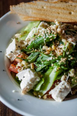 Tomato, cheese, lettuce, sesame, endive and cucumber salad with toasted bread in a plate on a wooden table