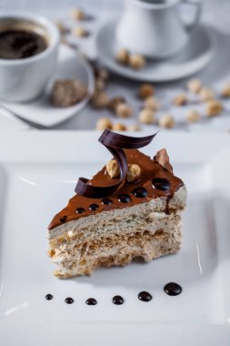 Waffle tabaklı bir dilim pasta çikolata jölesi, fındık, beyaz tabakta çikolata parçacıkları ve bir kupa kahve ve krema. Dikey yönelim