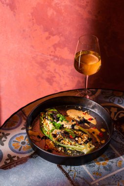 Fried salad with parsley, pepper, caviar, nuts and sauce in a plate on the table with a glass of wine