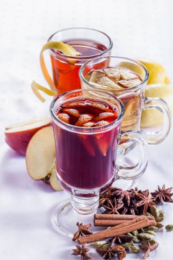 Baharatlı ve meyveli üç çeşit sıcak şarap. Elma dilimli beyaz şarap, portakal dilimli kırmızı şarap, limon aromalı gül şarabı. Bardakta içkiler, saplı bacaklarda şeffaf bardaklar. Yakınlarda...