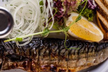 Fried mackerel, with potatoes, onion rings, lemon wedge, young shoots, salad and sauce. Horizontal orientation