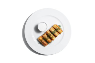 Rolled spring rolls, dill, sour cream in a plate on white background