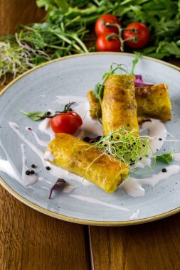 Mavi seramik tabakta, ekşi krema, mikroyeşil, vişneli domates ve fesleğen yapraklı gözleme. Parşömen ve süzme peynirli ahşap zemin, kiraz domates dalı, roka ve mikroyeşil.